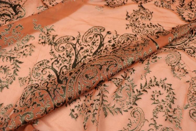 a close-up view of a fabric with a detailed, intricate paisley pattern in shades of orange and black. The pattern appears to be a decorative design, with the paisley motifs overlapping and creating a visually striking effect.