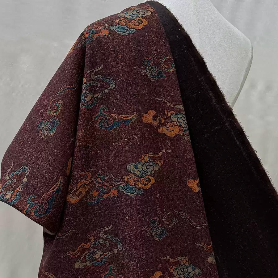 a close-up view of a dark-colored fabric with a pattern of clouds and swirls in shades of burgundy, orange, and blue.