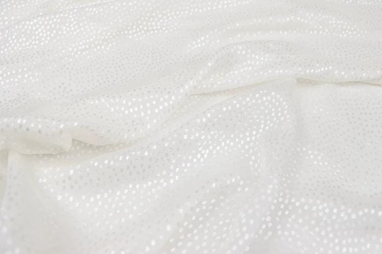 a close-up view of a white fabric with small white dots or sequins, creating a textured and shiny appearance.