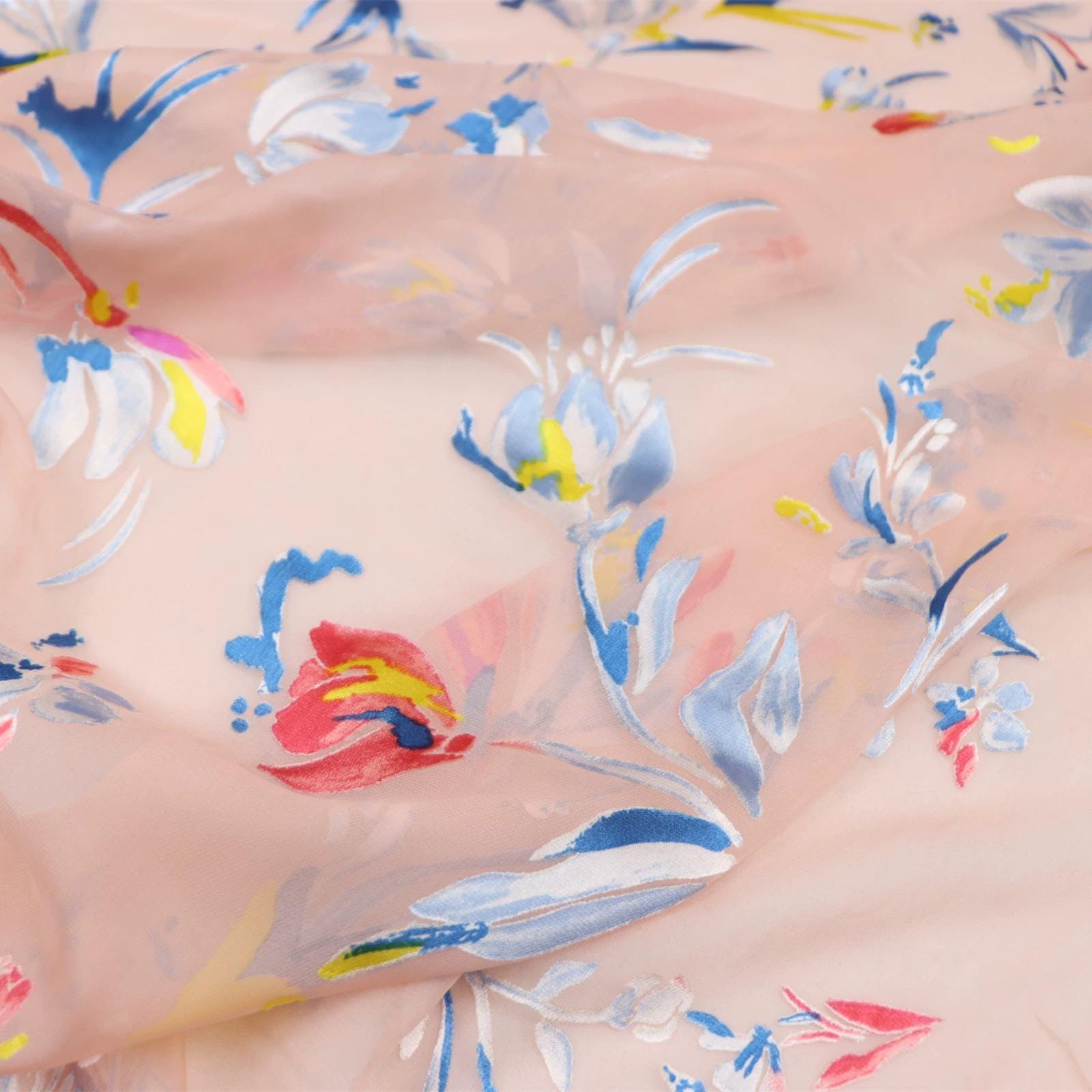 a close-up view of a fabric with a floral pattern. The fabric appears to be a light pink color, and the pattern consists of various flowers and leaves in different colors, including blue, yellow, and white. The fabric is crumpled, giving it a soft and delicate appearance.