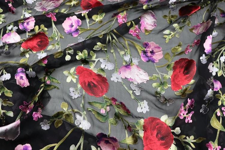 a close-up view of a fabric with a floral pattern. The fabric is predominantly black, with red and white flowers, including red roses, scattered across the surface. The flowers are arranged in a way that creates a visually appealing and intricate design.
