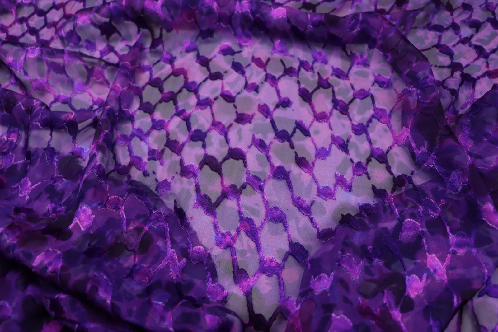 a close-up view of a fabric with a purple and pink pattern, featuring a repeating geometric design.