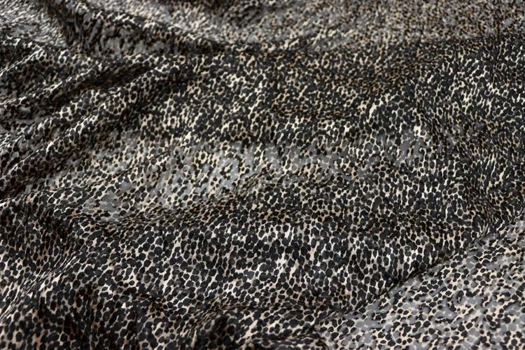 a close-up view of a fabric with a distinctive leopard print pattern. The fabric appears to be a dark-colored material with a mix of black and white spots, resembling the fur of a leopard. The pattern is intricate and detailed, creating a visually striking and textured appearance.