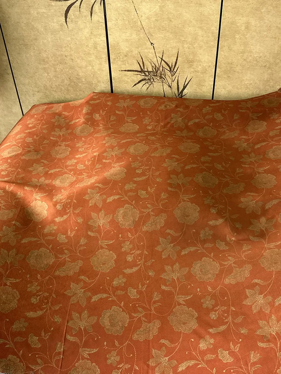 a close-up view of a red and gold floral patterned fabric, possibly a bedspread or pillowcase, with a decorative wall panel featuring a floral design in the background.