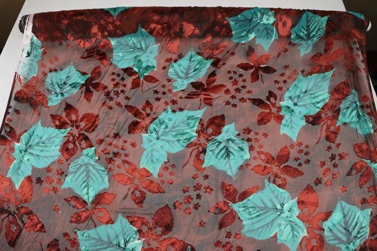 a fabric with a vibrant floral pattern of red and green leaves and flowers. The pattern is spread across the fabric, creating a visually striking and colorful design.