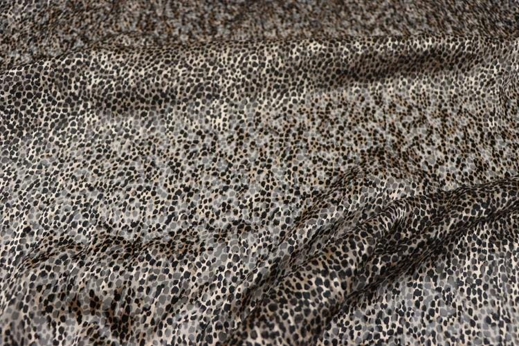a close-up view of a fabric with a leopard print pattern, featuring a mix of brown and black spots.