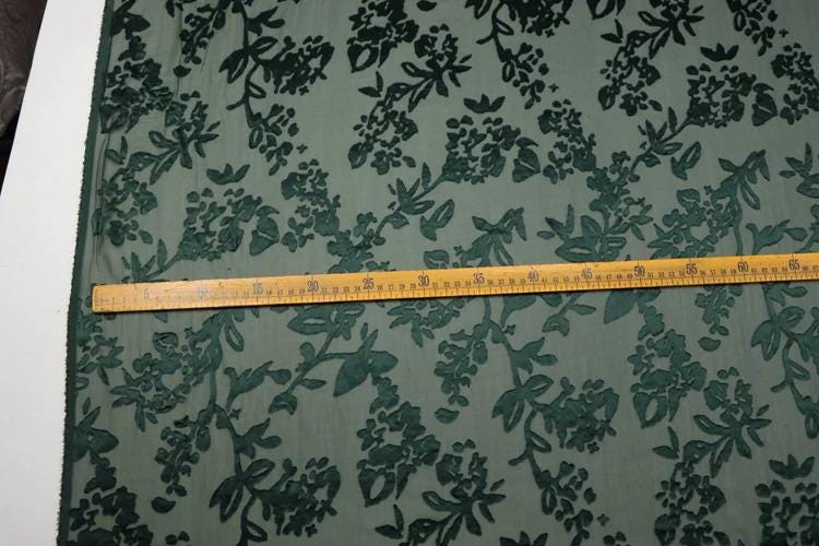a close-up view of a fabric with a floral pattern, and a ruler is placed across it to measure the length of the fabric.