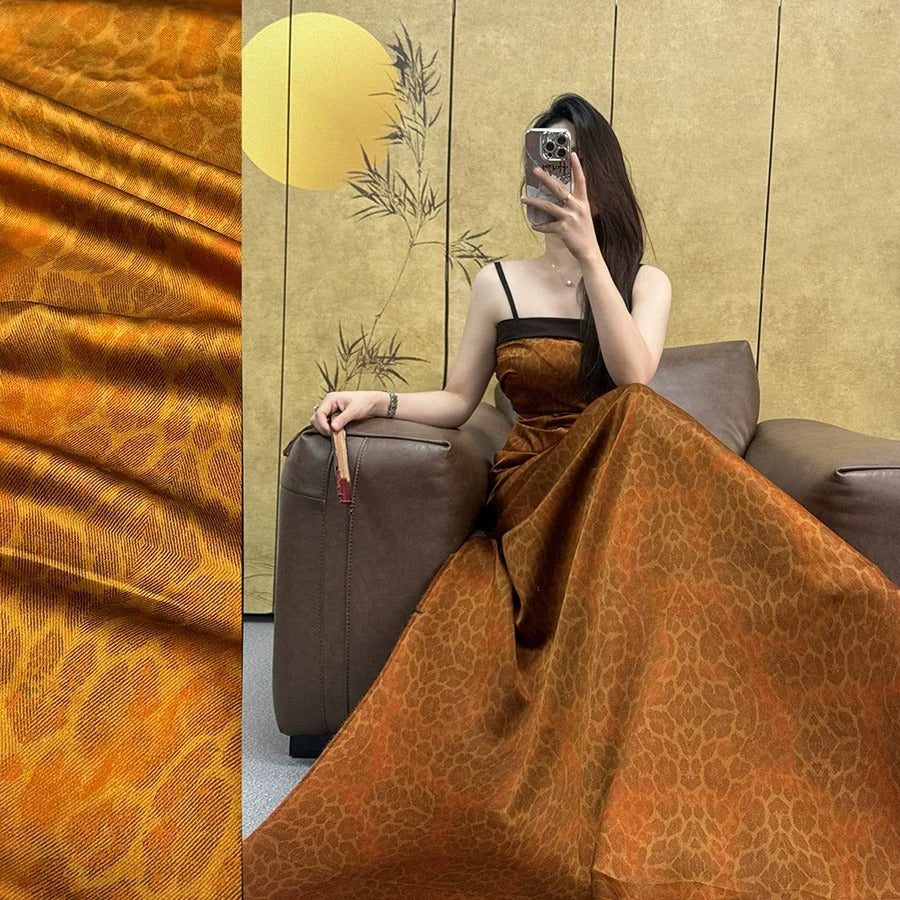 A woman in a long, orange dress is sitting on a couch, holding a phone up to her face.