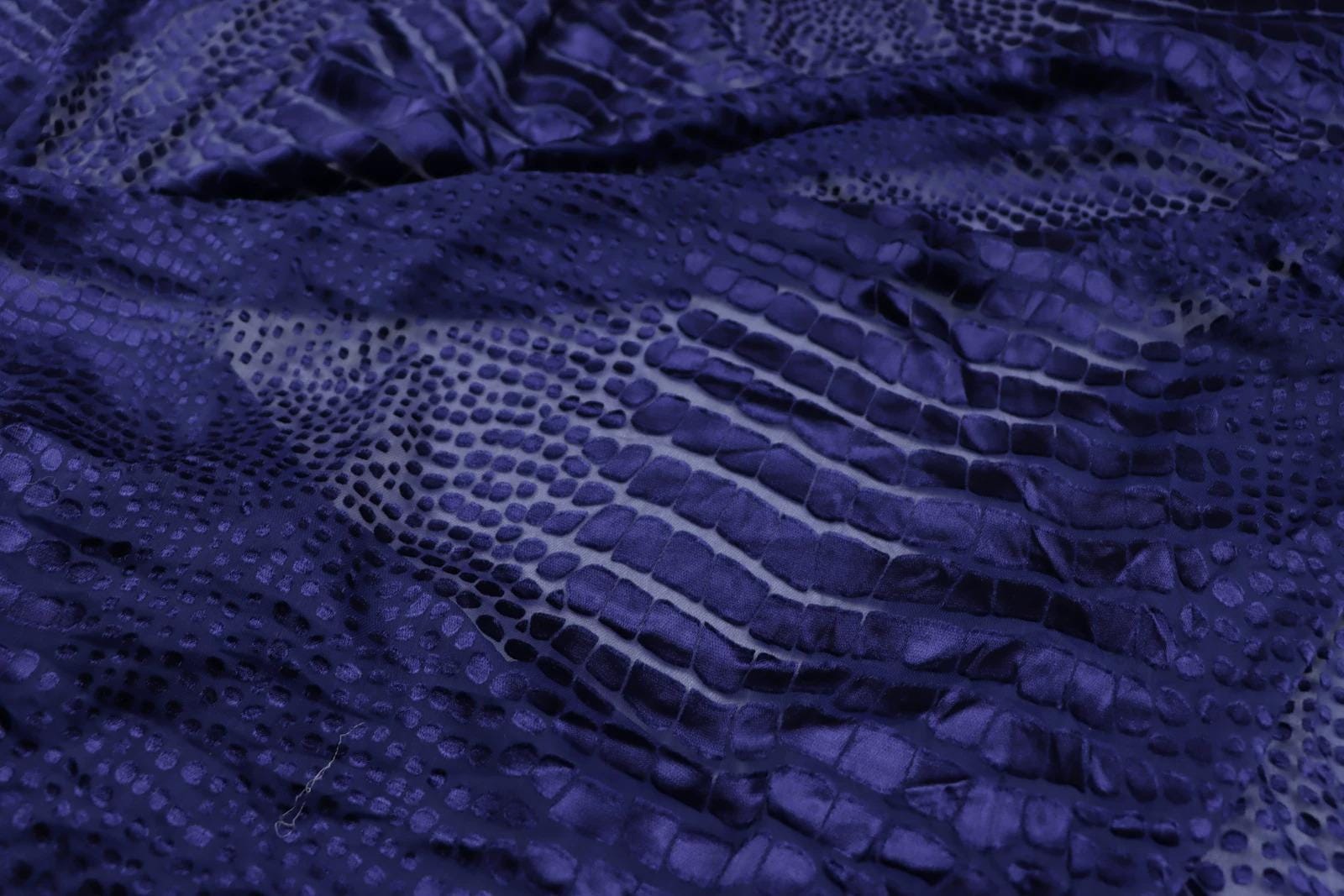 a close-up view of a fabric with a distinctive pattern resembling scales or scales, giving it a textured and shiny appearance.