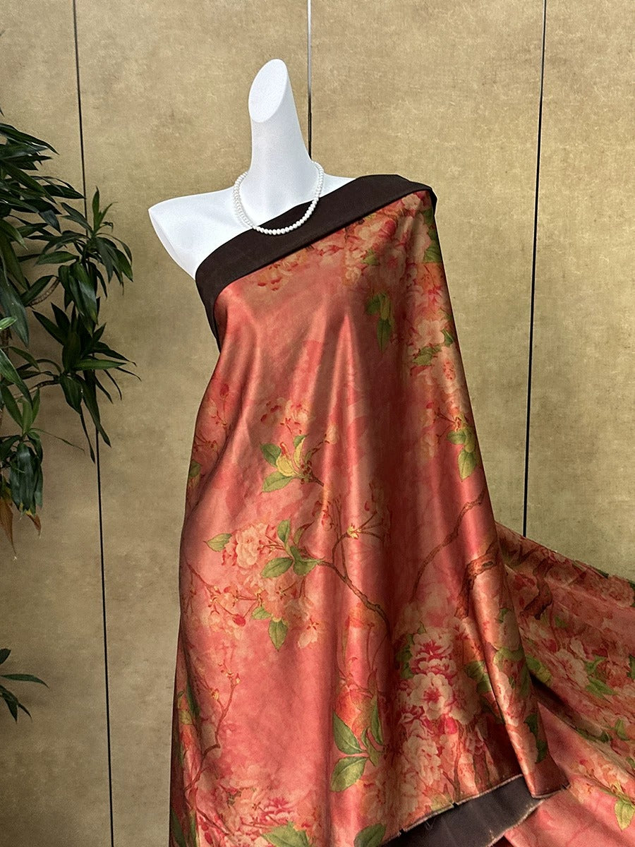 A mannequin wearing a red and green floral print dress with a brown top, displayed against a beige wall with a plant in the background.