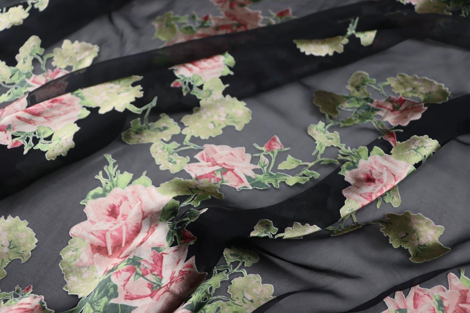 a close-up view of a fabric with a floral pattern, featuring pink and green flowers against a dark background.