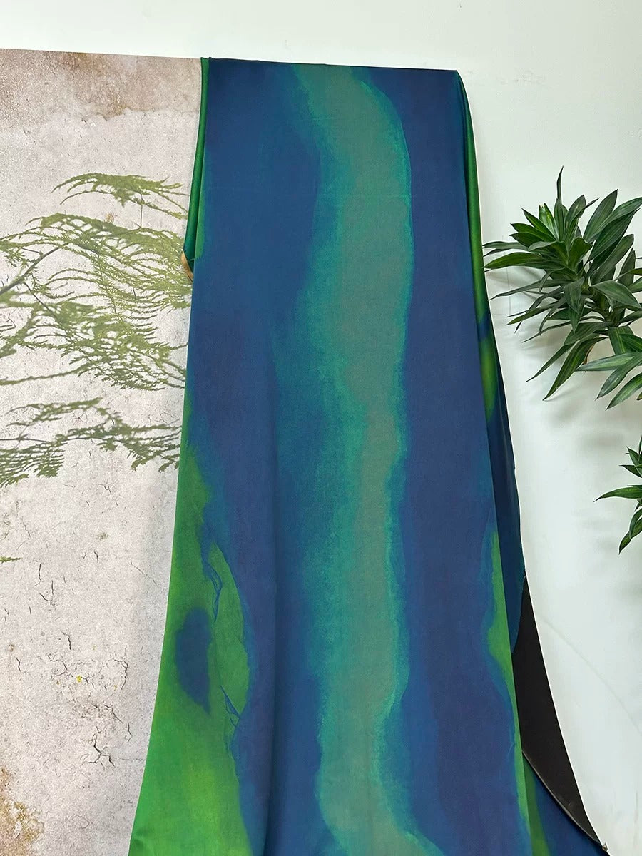 a large piece of fabric with a vibrant blue and green color gradient, hanging on a wall next to a plant.