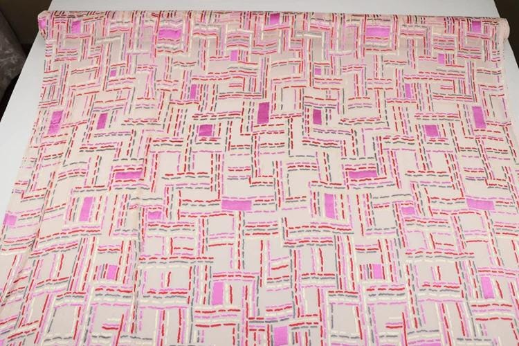 a fabric with a geometric pattern in shades of pink and white, featuring a repeating pattern of squares and rectangles.