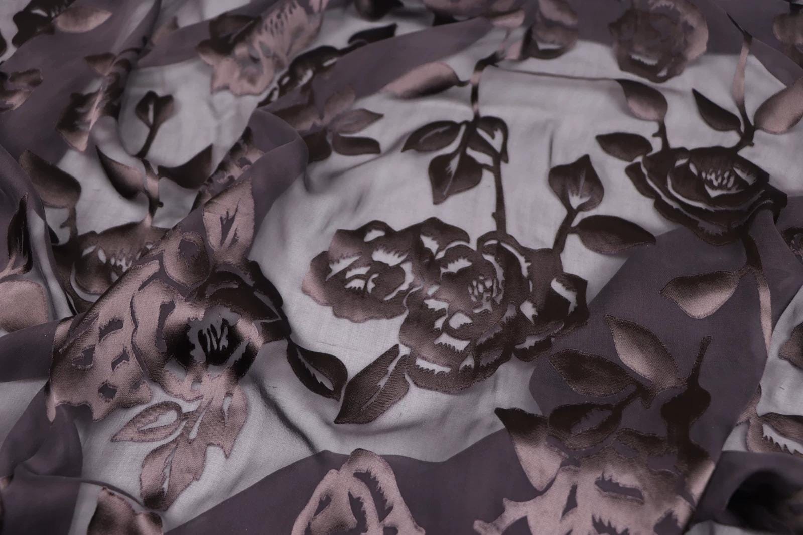 a close-up view of a fabric with a floral pattern, featuring a mix of dark and light colors. The pattern consists of various shades of brown and gray, with some areas of black and white. The fabric appears to be made of a soft, silky material, and the intricate design of the flowers and leaves adds a sense of detail and texture to the image.