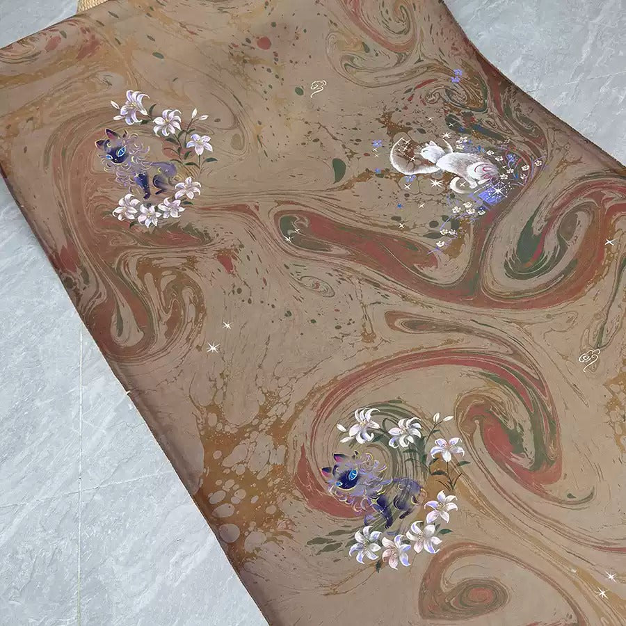 a close-up view of a textured fabric with a floral pattern. The fabric has a marbled effect, with swirls and splatters of color creating a visually interesting design. There are also small white flowers and a cat-like creature, adding to the overall aesthetic of the fabric.