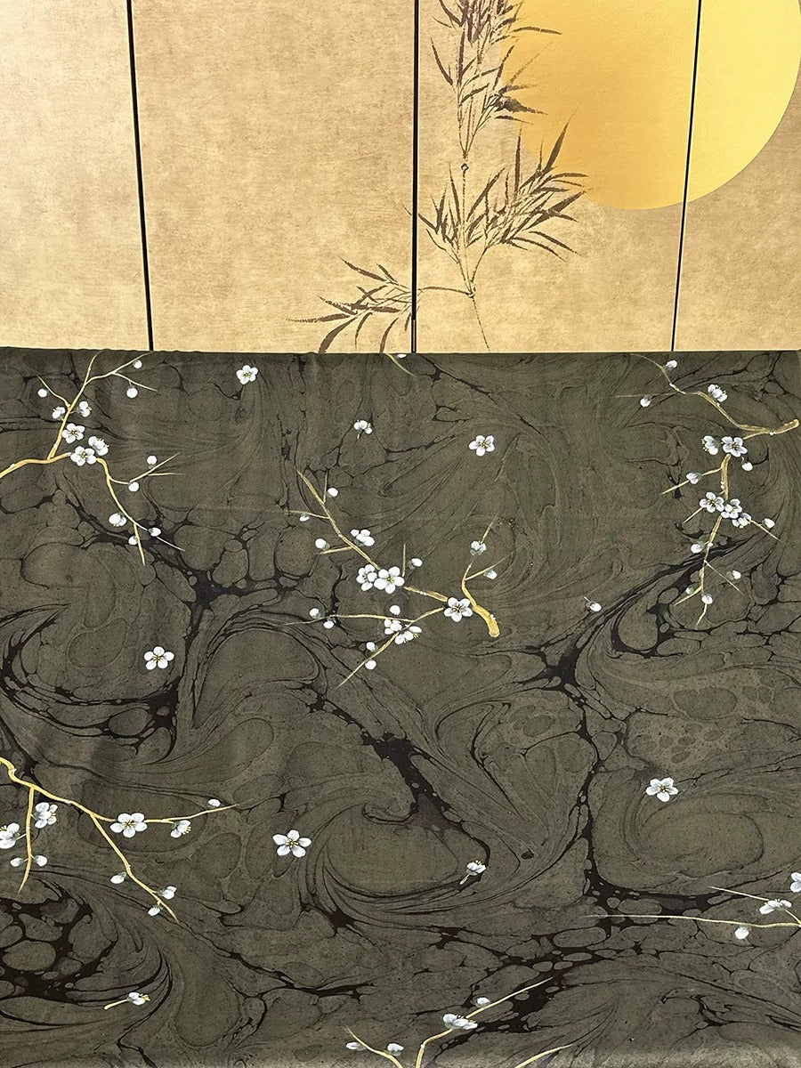 a close-up view of a dark, textured surface with white flowers and branches scattered across it. The background is a light brown color, with a yellow circle visible in the top right corner.
