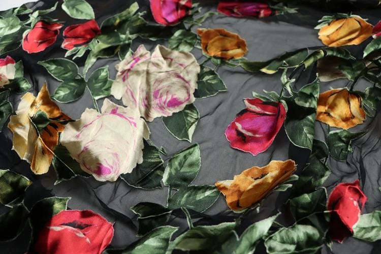 a close-up view of a fabric with a floral pattern, including red, pink, and yellow flowers. The fabric appears to be black, with the flowers and leaves covering the entire surface.