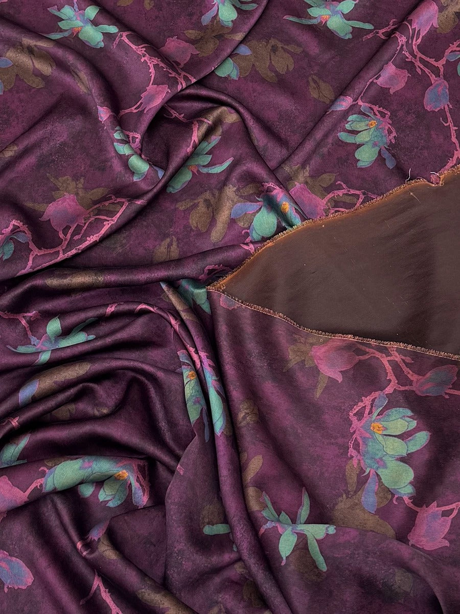 a close-up view of a fabric with a floral pattern in shades of purple and green. The fabric appears to be crumpled and wrinkled, giving it a textured and soft appearance.