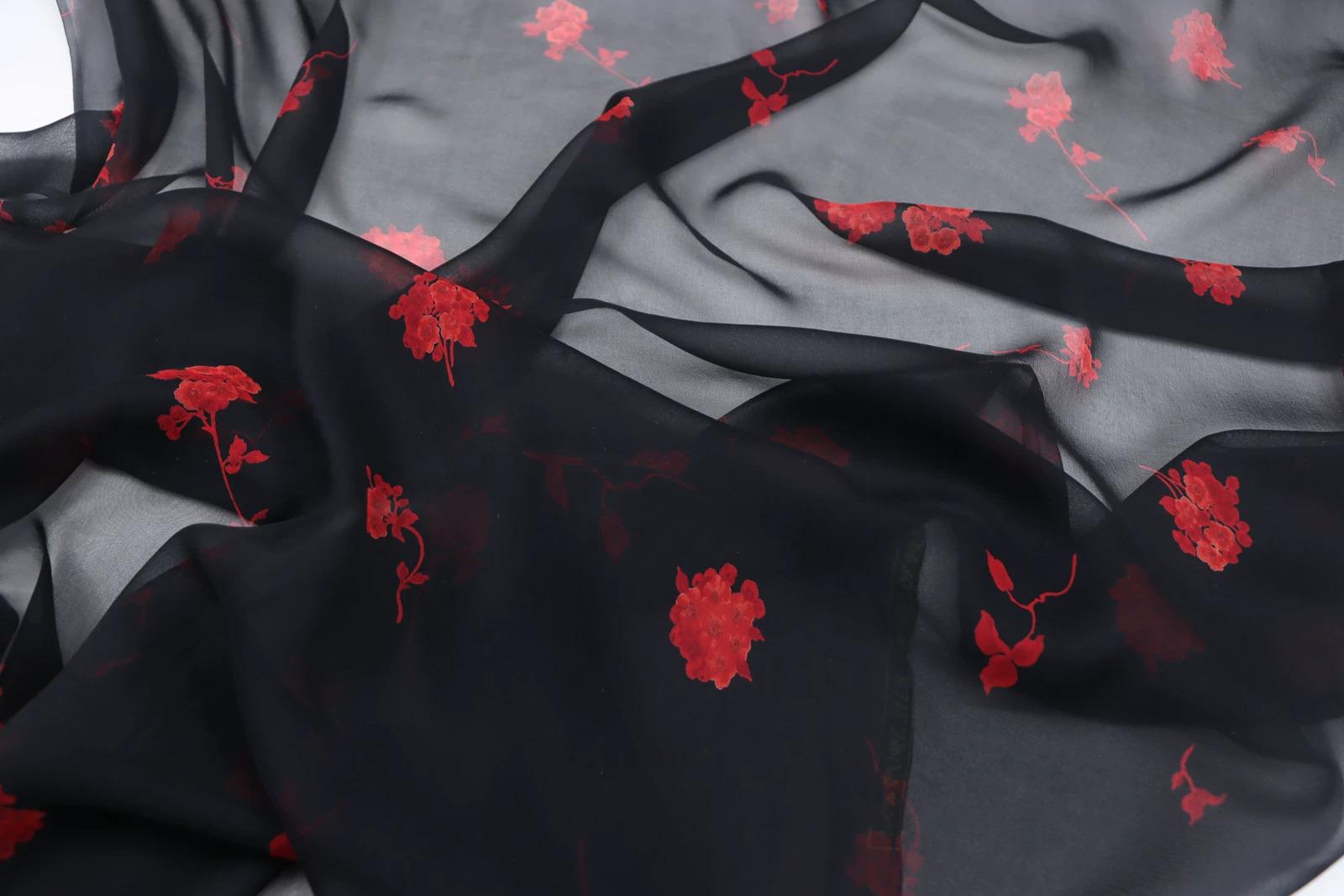 a close-up view of a black fabric with red floral embroidered patterns. The fabric appears to be made of silk or chiffon, and the red flowers are visible on the fabric, creating a visually striking contrast against the black background.