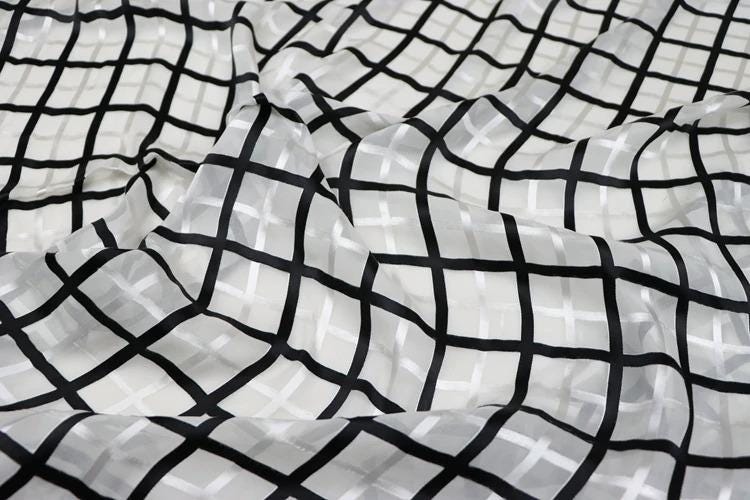 a close-up view of a fabric with a black and white checkered pattern. The fabric appears to be made of a sheer material, with a grid-like design that creates a visually striking pattern.