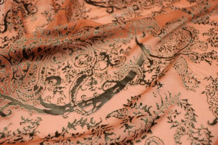 a close-up view of a fabric with a detailed, intricate paisley pattern in shades of orange and black.