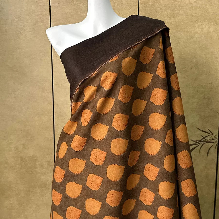 A mannequin wearing a brown and orange patterned fabric draped over its shoulder.