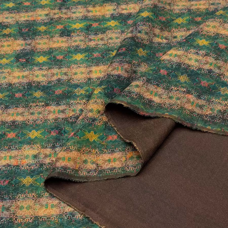 a close-up view of a fabric with a colorful, patterned design. The fabric appears to be a blend of green, yellow, and brown colors, with a repeating pattern of geometric shapes and lines. The fabric is folded and partially unrolled, revealing the intricate design underneath.