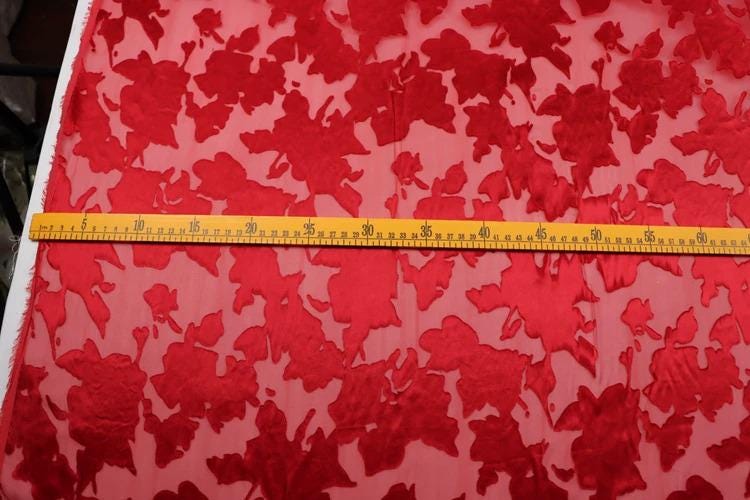 a red fabric with a floral pattern, and there is a yellow ruler placed on top of it, indicating the size of the fabric.