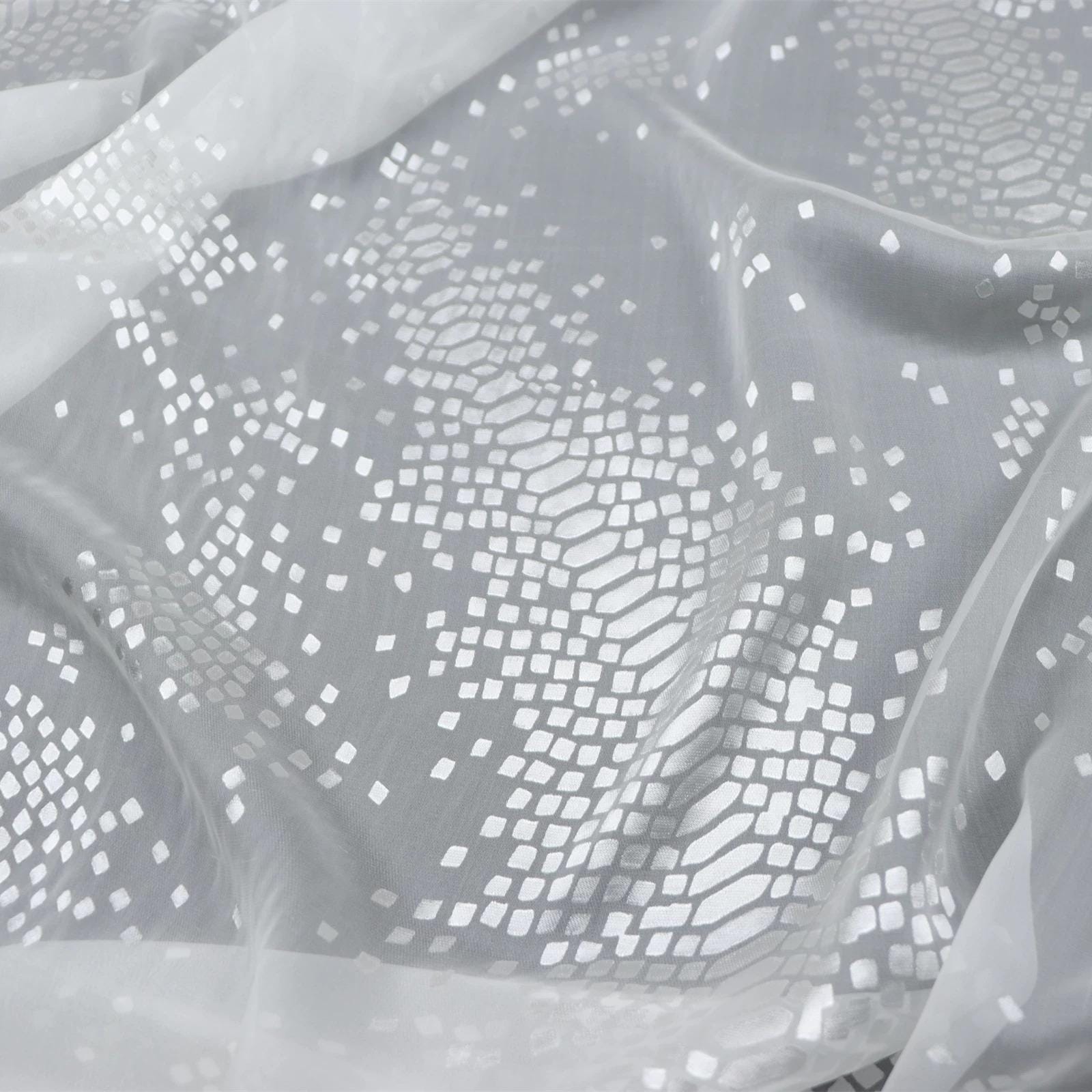 a close-up view of a fabric with a white, diamond-shaped pattern. The fabric appears to be made of a soft, flowing material, possibly chiffon or sheer. The pattern consists of numerous small white diamonds arranged in a repeating geometric design, creating a visually striking and intricate appearance.