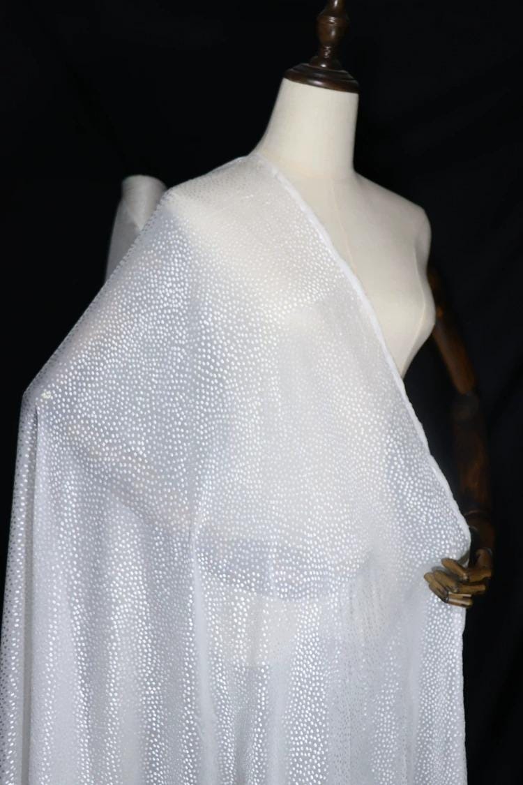 A mannequin wearing a white, sheer fabric with a metallic, sparkly texture.