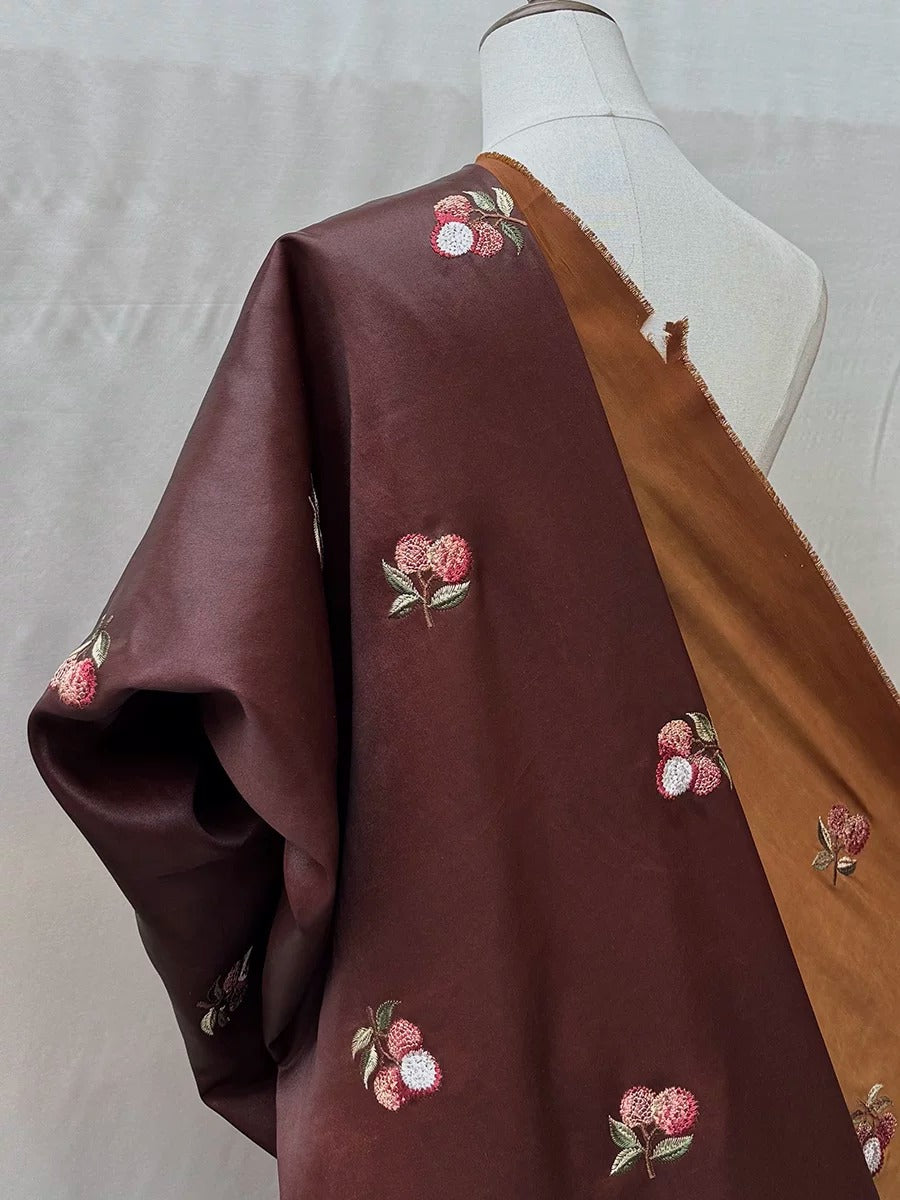 A mannequin wearing a burgundy fabric with a brown trim, featuring a repeating pattern of small floral designs in shades of red and brown.