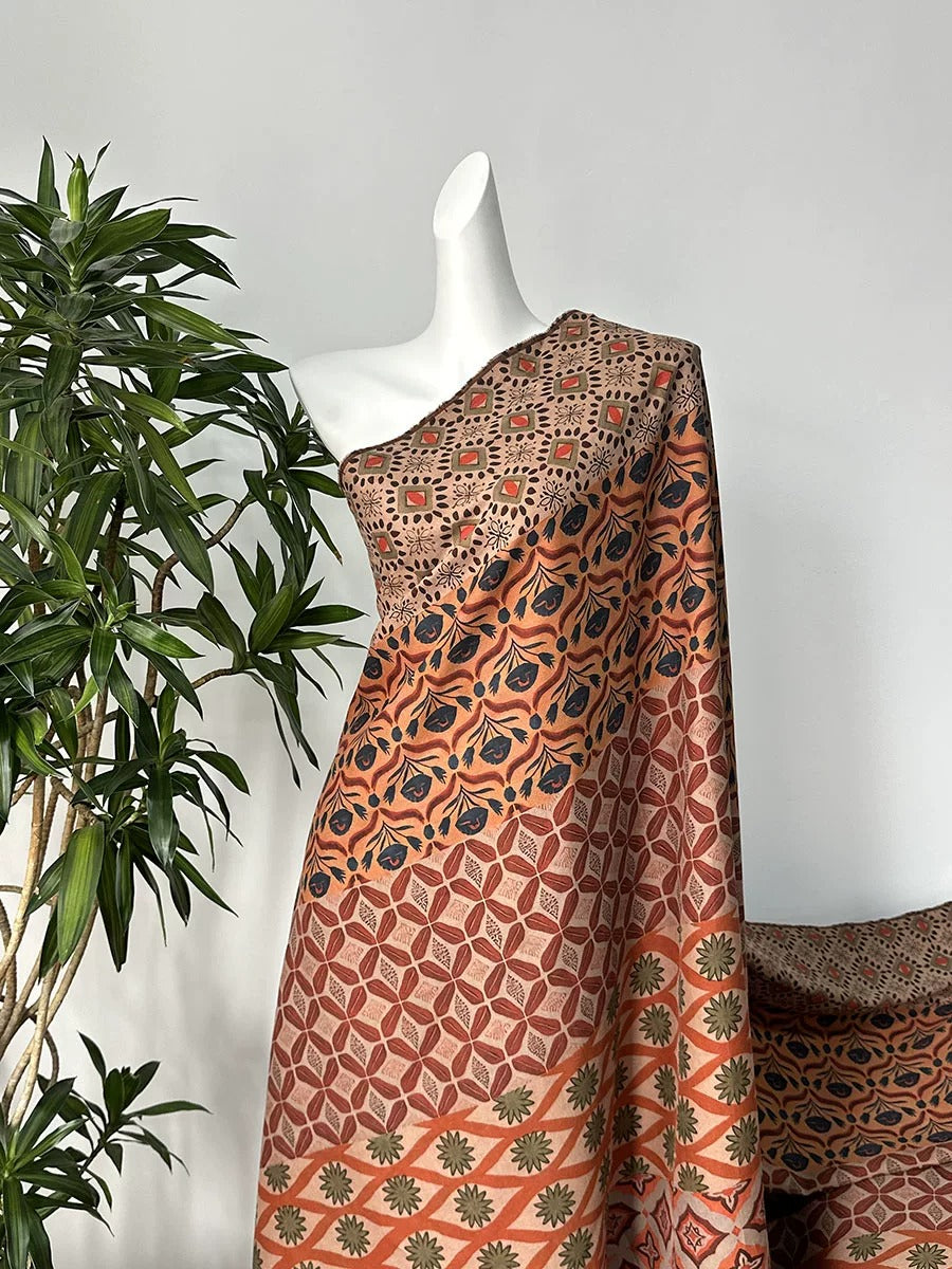 a mannequin wearing a colorful, patterned dress with a floral design. The dress has a one-shoulder style and is displayed against a plain white wall. A potted plant is visible in the background, adding a touch of greenery to the scene.
