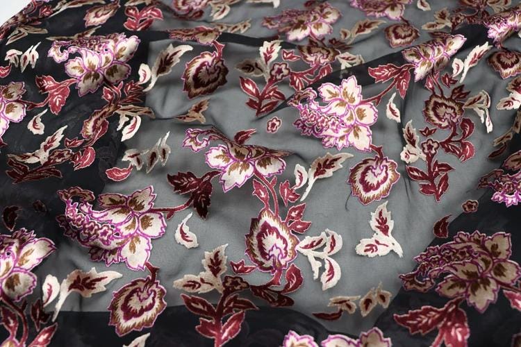 a close-up view of a fabric with a floral pattern in shades of pink, red, and white. The fabric appears to be a sheer material, with a dark background that highlights the colorful floral design.