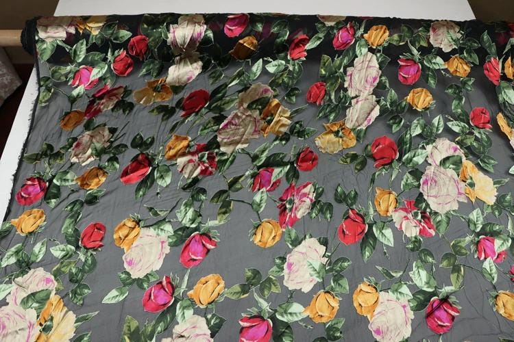 a close-up view of a fabric with a floral pattern of red, yellow, and white roses against a dark background.
