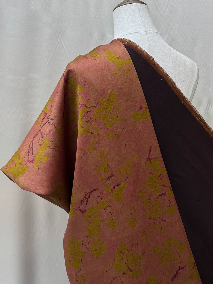 a mannequin wearing a dress with a vibrant floral print in shades of pink and yellow. The dress has a dark brown fringe on the sleeves, creating a striking contrast with the colorful fabric.