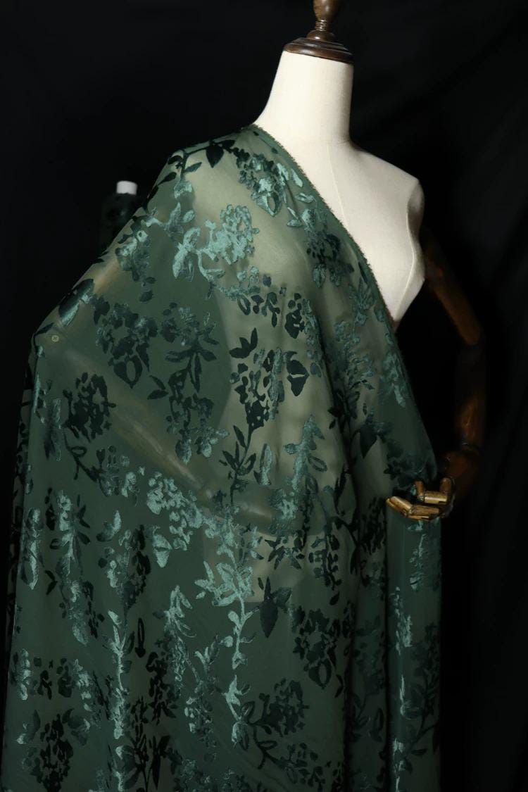 A mannequin wearing a green fabric with a floral pattern, displayed against a black background.