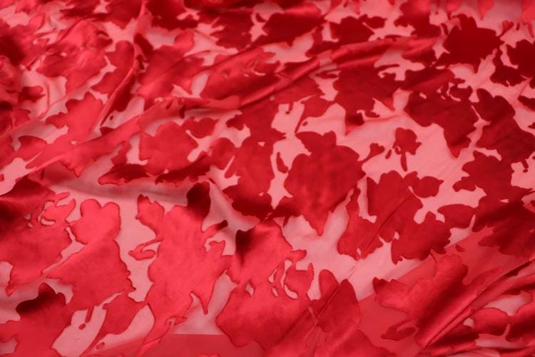 The image is a close-up of a red fabric with a floral pattern, featuring a repeating design of red flowers or leaves.