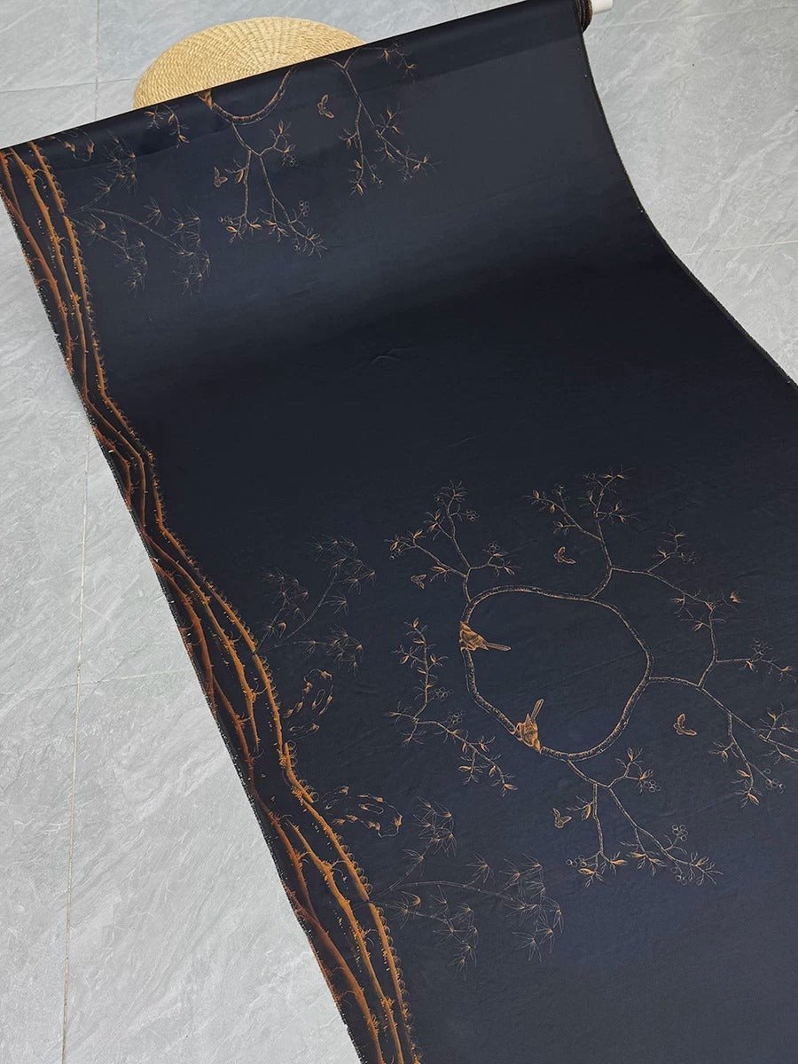 a black fabric with a gold leaf design, including a tree-like pattern and a circular design. The fabric appears to be rolled up and placed on a gray tile floor.