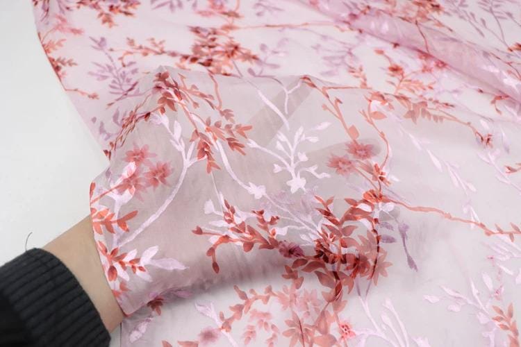 A close-up view of a hand holding a fabric with a floral pattern in shades of pink and red.