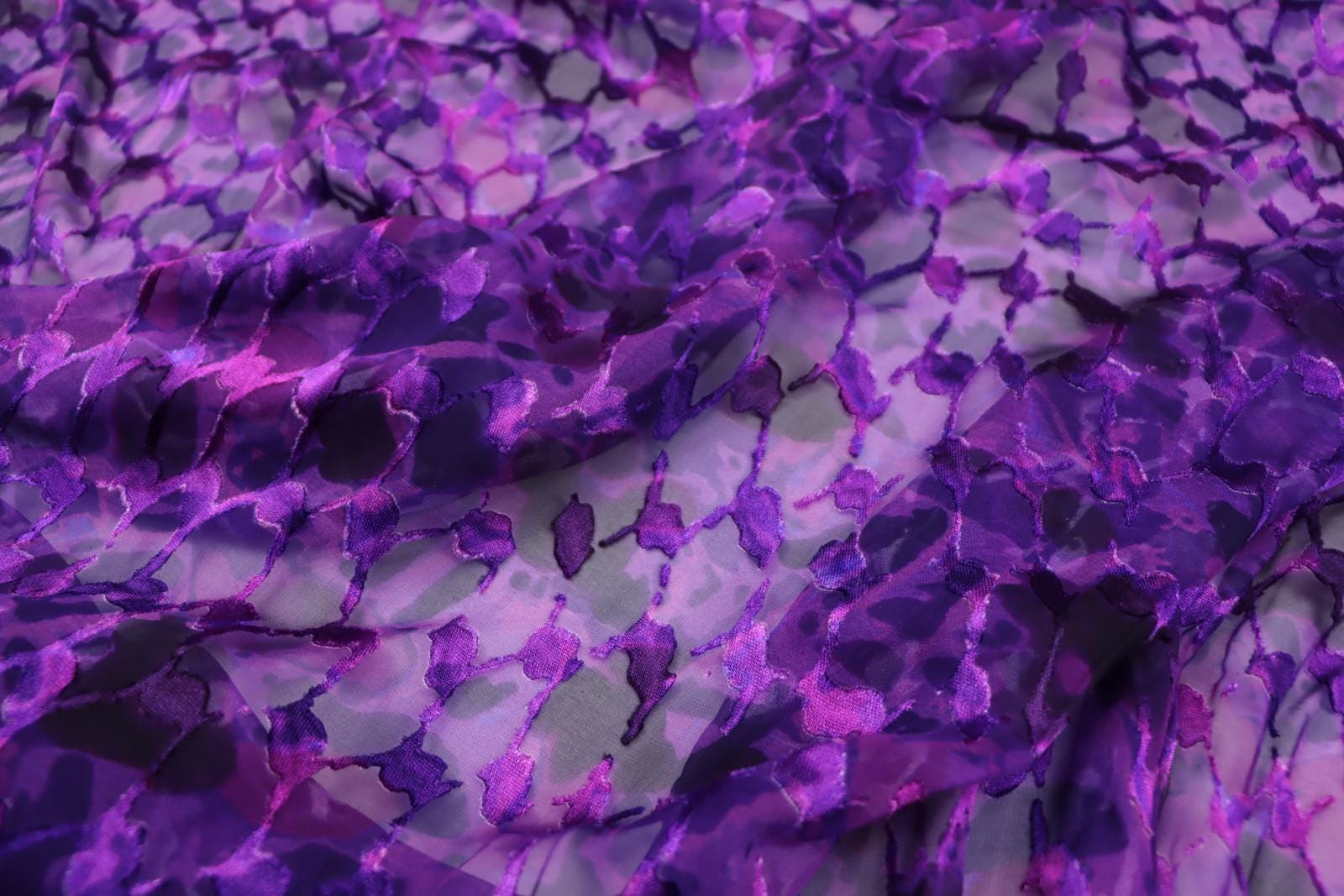 a close-up view of a fabric with a purple and black pattern, featuring a repeating design of purple and black shapes.