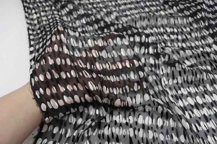 a close-up view of a hand holding a piece of fabric with a black and white polka dot pattern.