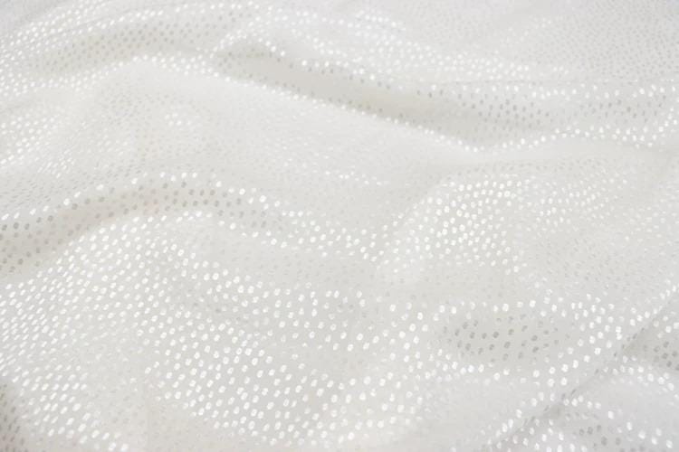 a close-up view of a white fabric with small white dots or polka dots, creating a textured and shiny appearance.