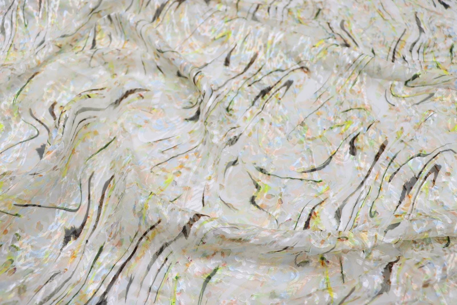The image is a close-up of a fabric with a colorful, abstract pattern of lines and swirls in various shades of white, yellow, and green.