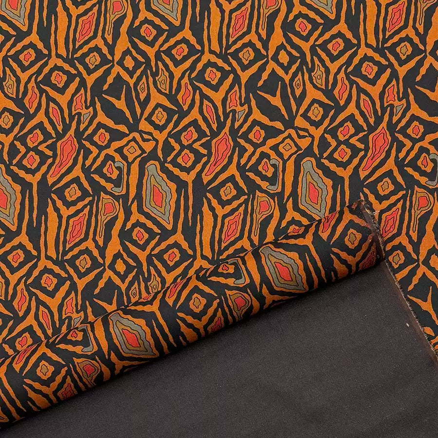 a close-up view of a fabric with a striking geometric pattern in shades of orange, black, and gray. The pattern consists of numerous diamond-shaped motifs arranged in a repeating pattern, creating a visually captivating design. The fabric appears to be a piece of cloth or textile, with the intricate pattern suggesting it could be used for various purposes, such as clothing, home decor, or art.