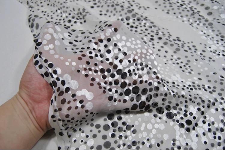 A hand is holding a piece of fabric with a black and white polka dot pattern.