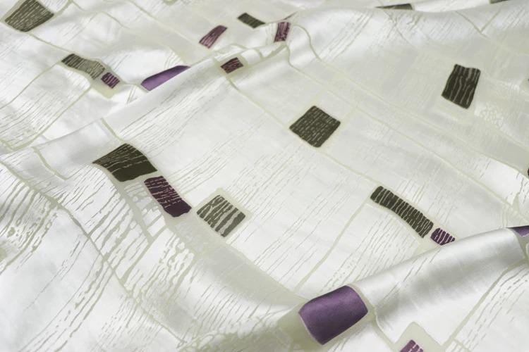 a close-up view of a white fabric with a pattern of purple and black squares or rectangles.