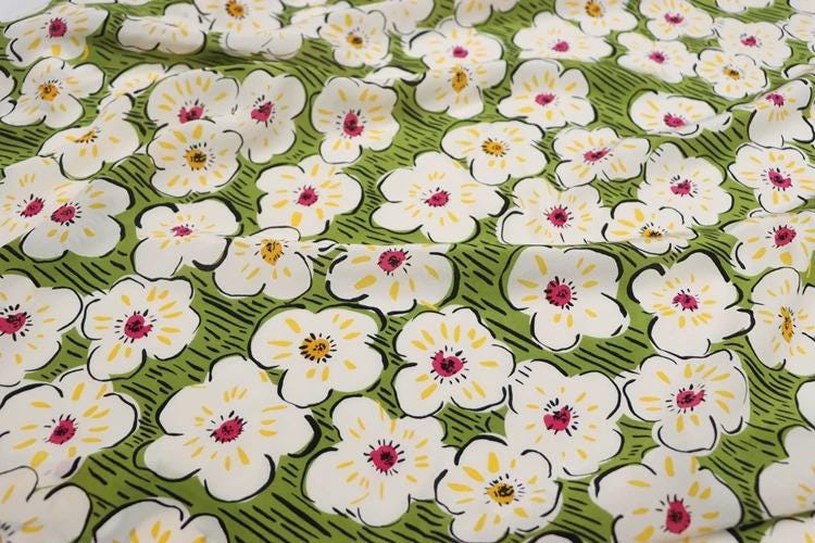 a close-up view of a fabric with a repeating pattern of white flowers with yellow centers and pink centers against a green background.