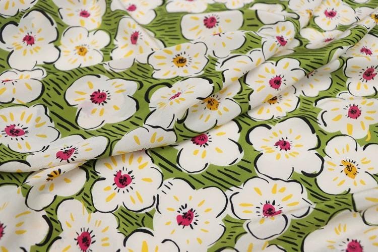 a close-up view of a fabric with a repeating pattern of white flowers with yellow centers against a green background.