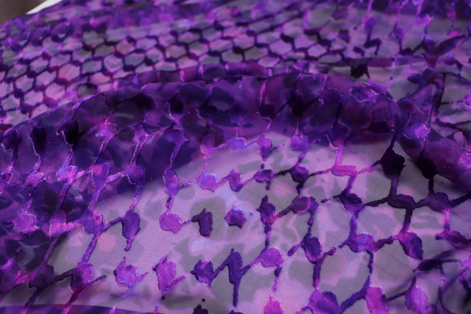 a close-up view of a fabric with a purple and black pattern, featuring a repeating geometric design.