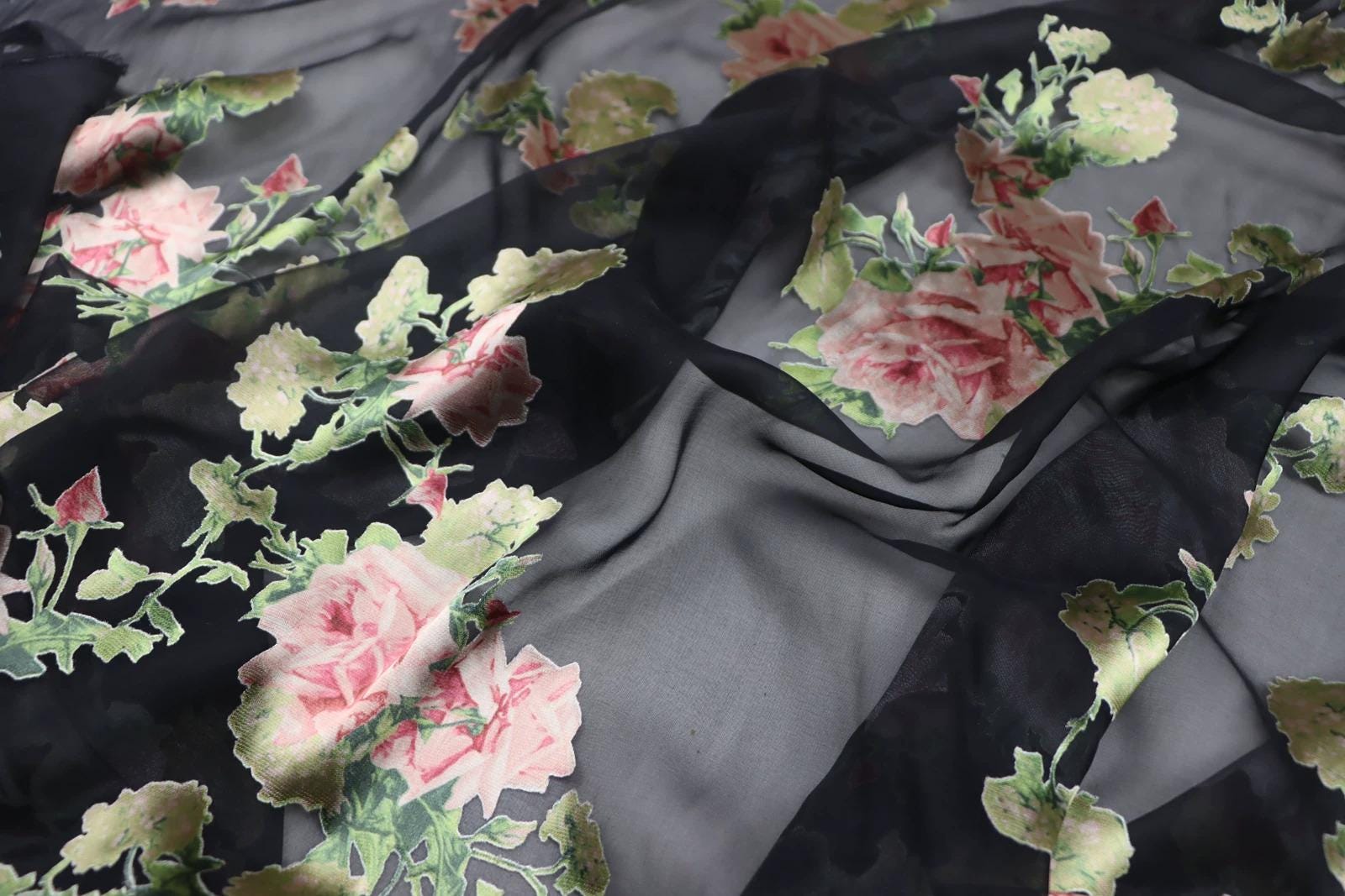 a close-up view of a fabric with a floral pattern, featuring pink and green flowers against a black background.